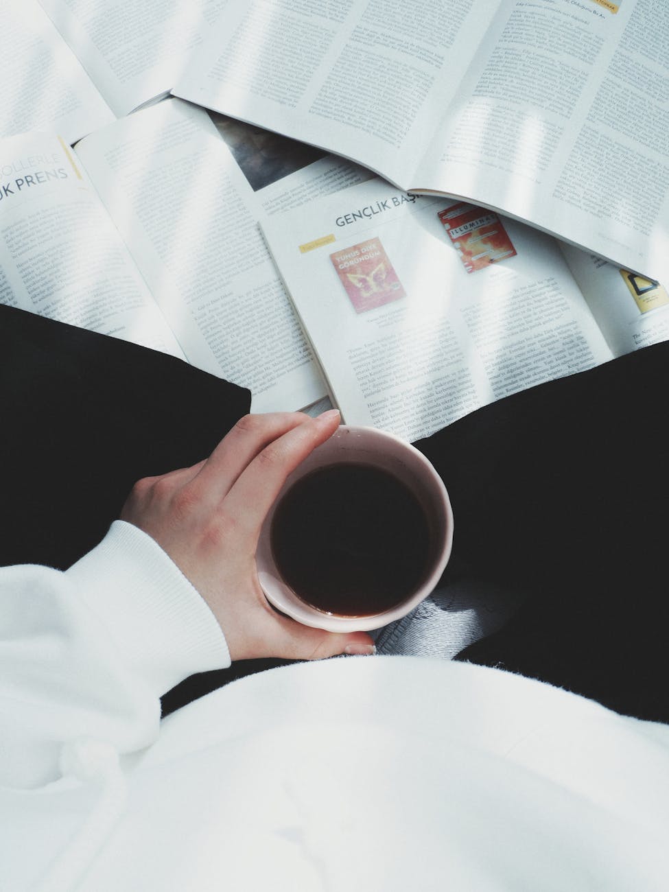 cup of coffee held by a woman sitting among magazines